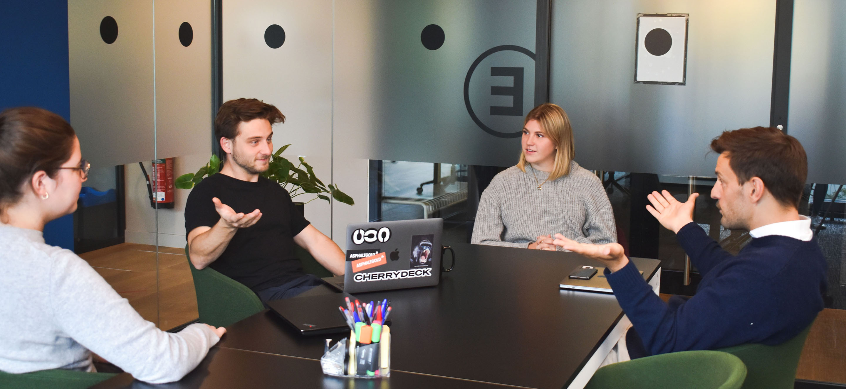 Team of four people talking at a table in an office.