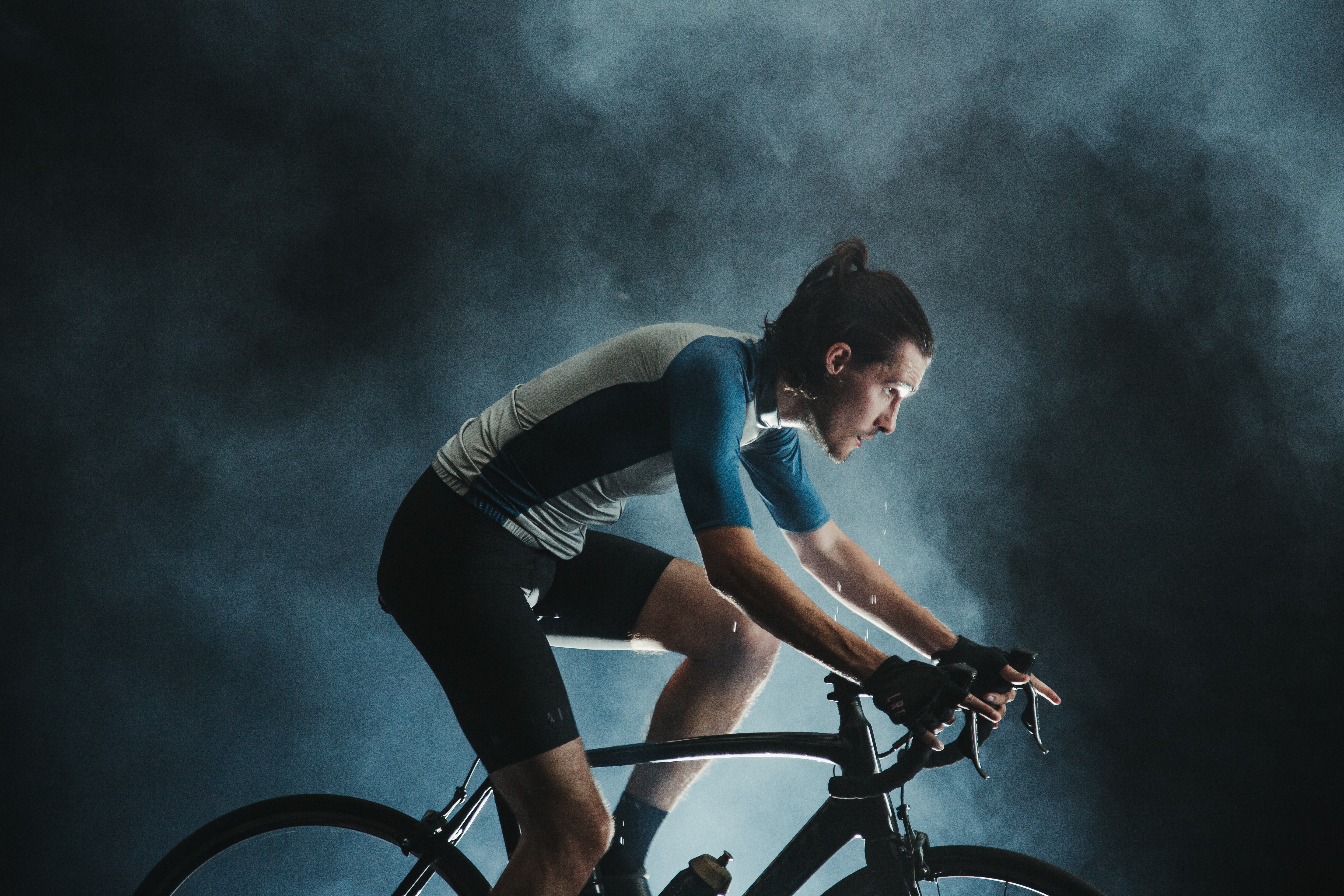 man in spotlight with cloudy backdrop riding a stationary bike