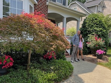 Clint and Abby Morrison standing in front of their home and flower
                garden
