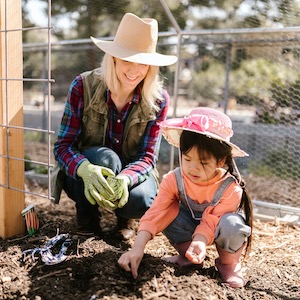 woman and child squatting in garden planting seeds together