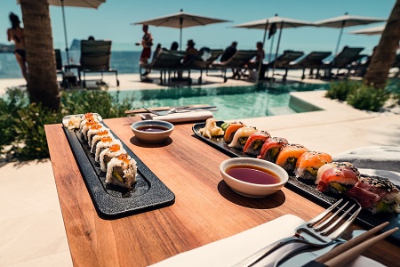 display of sushi on table next to a pool with a crowd on the background