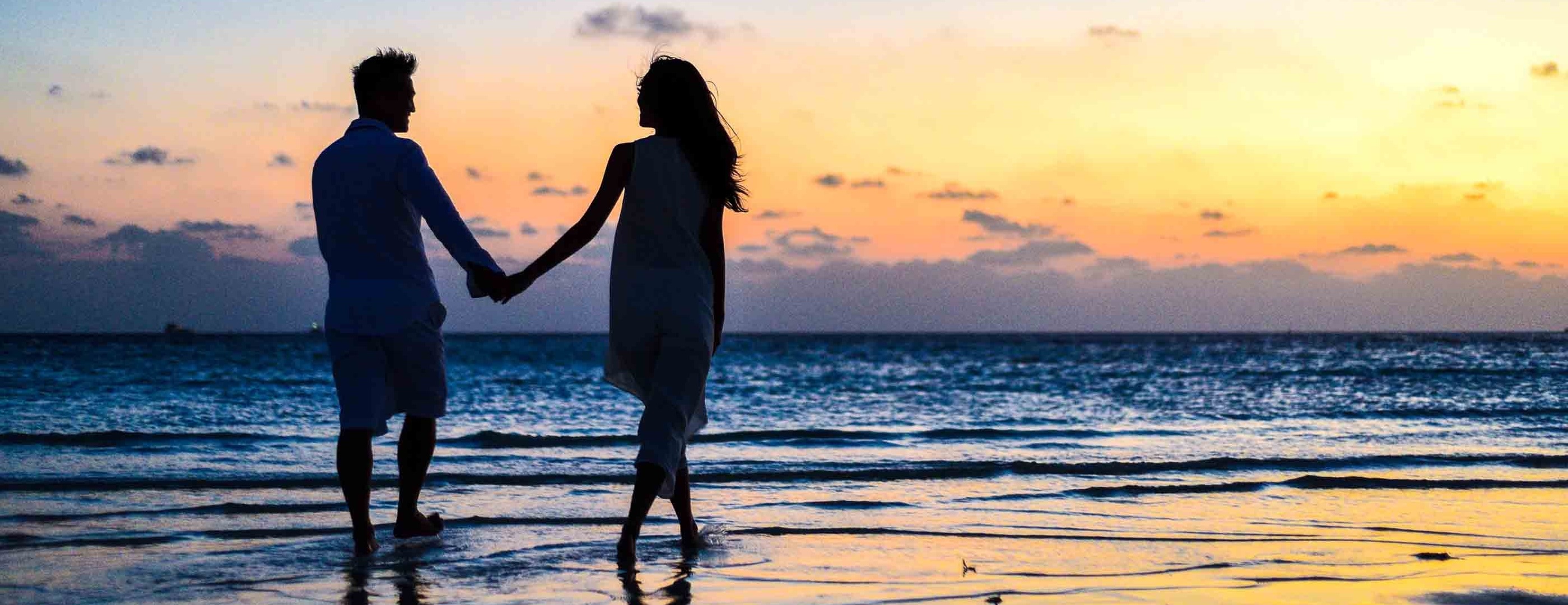 couple holding hands, walking late evening on a beach