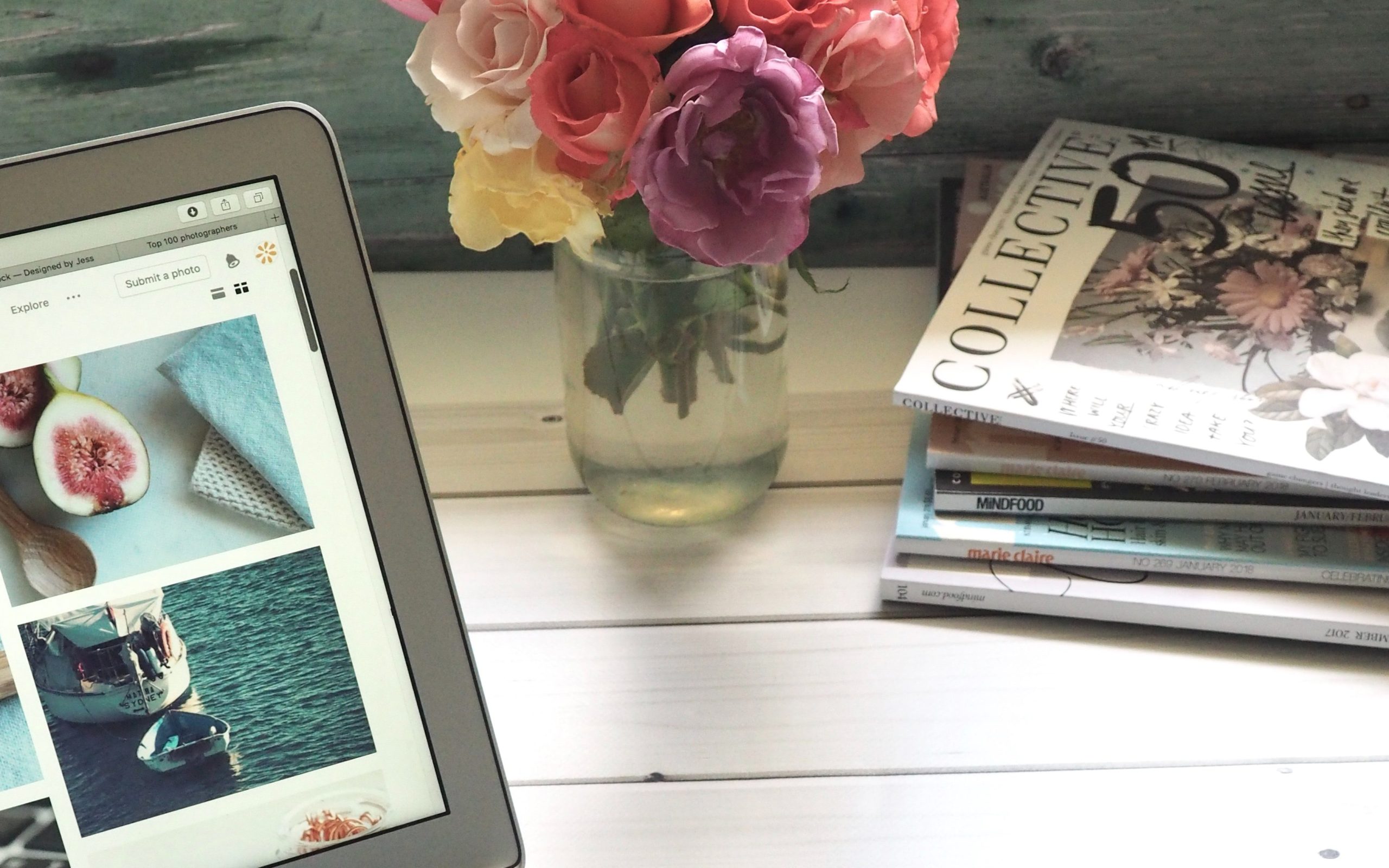 Compute, vase of beautiful flowers, and magazines on wooden desk.