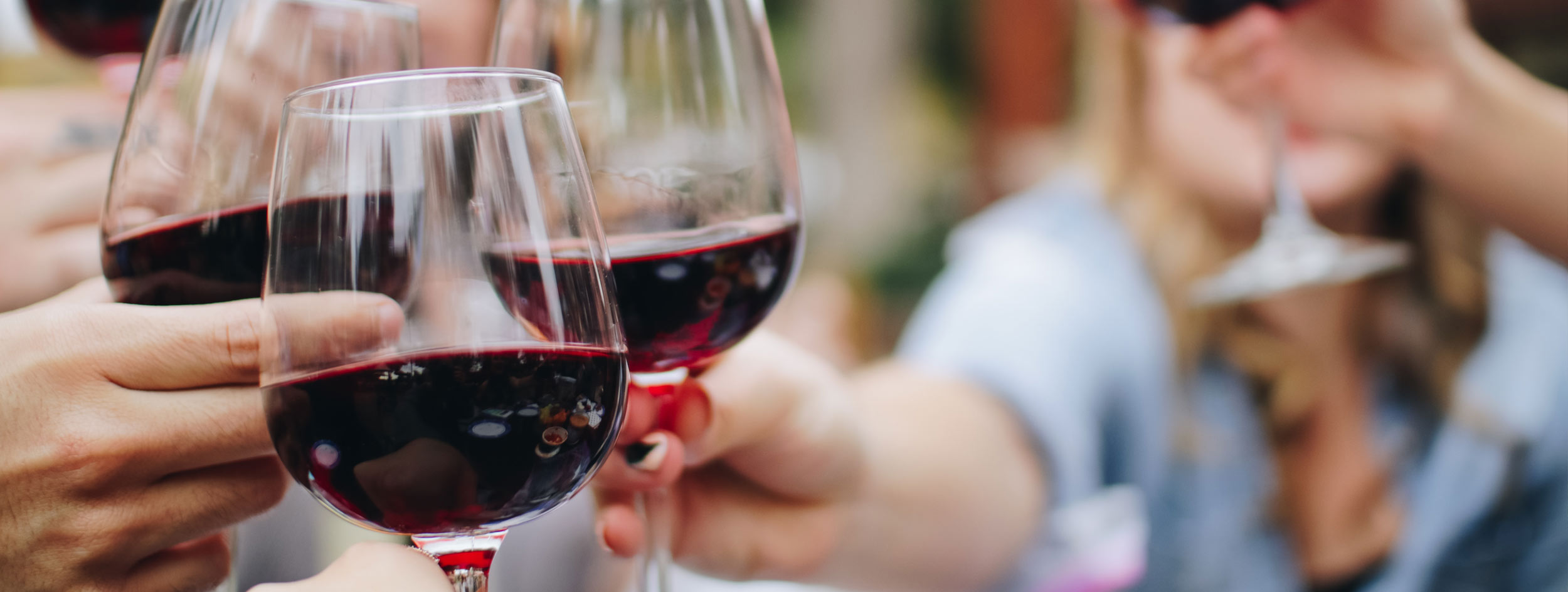 People clinking wine glasses filled with red wine.