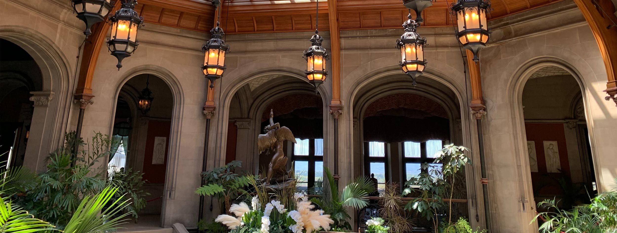 The front of the Biltmore house with people outside and on the lawn on a partially cloudy fall afternoon.