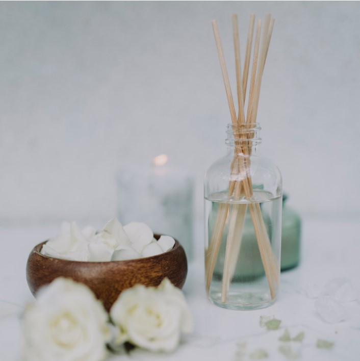 diffusing sticks in a transparent bottle with white rose petals on a table